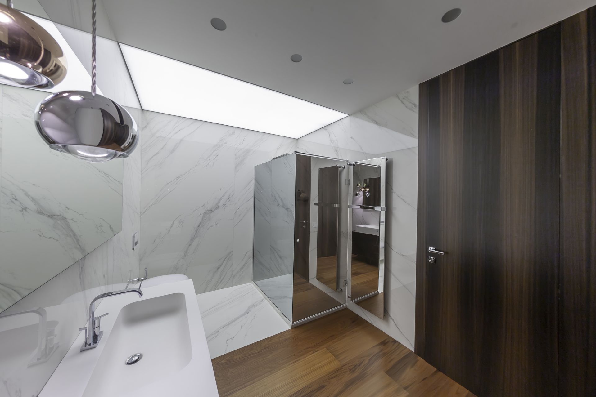 Bagno moderno con pareti in marmo, pavimento in legno, accessori cromati e doccia con cabina in vetro.