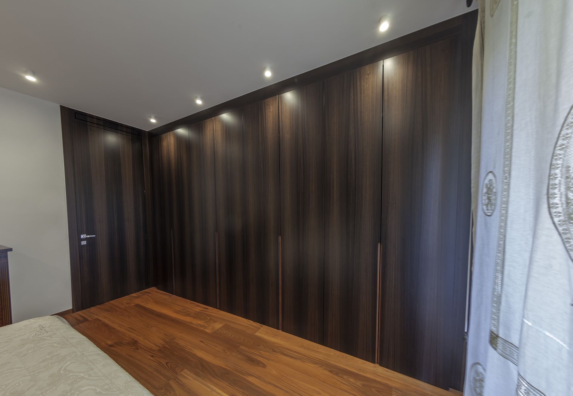 Camera da letto con armadio a muro in legno scuro, pavimenti in legno e luci al soffitto.