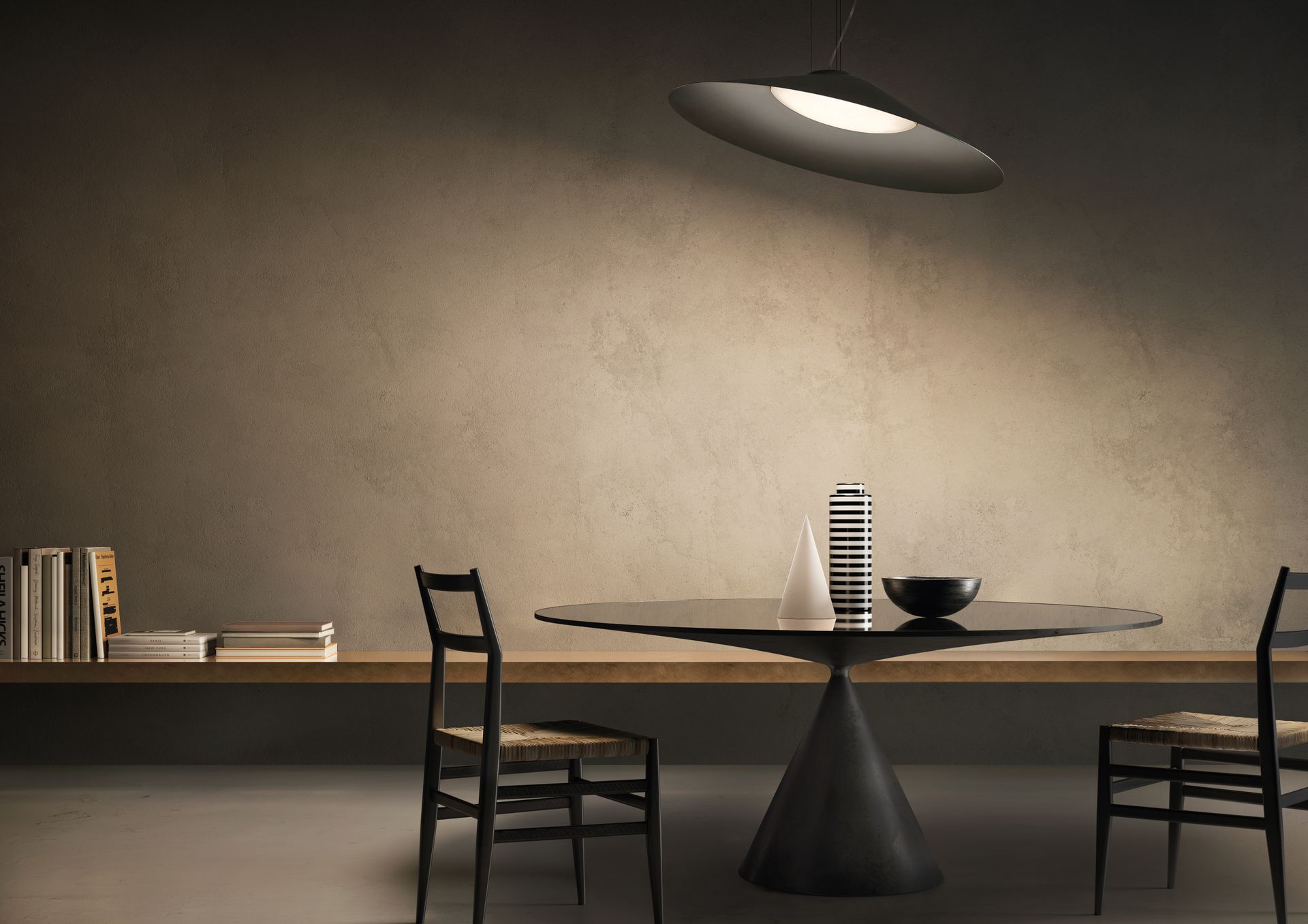 Sala da pranzo: tavolo rotondo nero, due sedie, lampada a sospensione, libreria e parete.