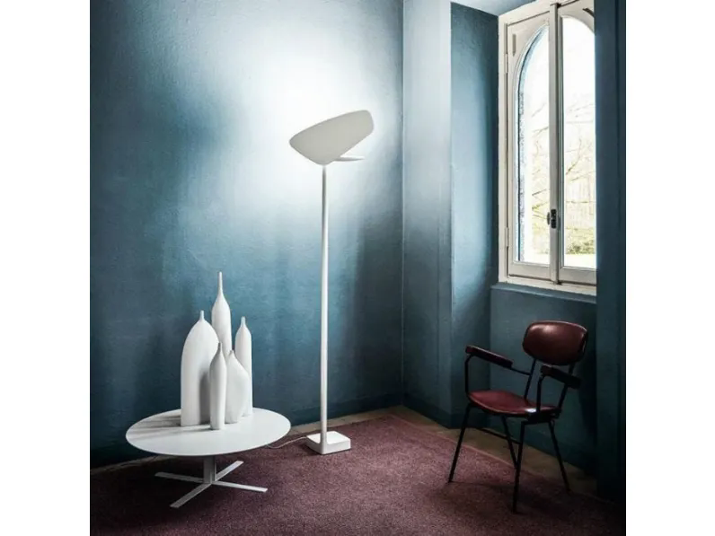 Lampada da terra bianca, tavolino con vasi e sedia in una stanza con pareti blu e una finestra.