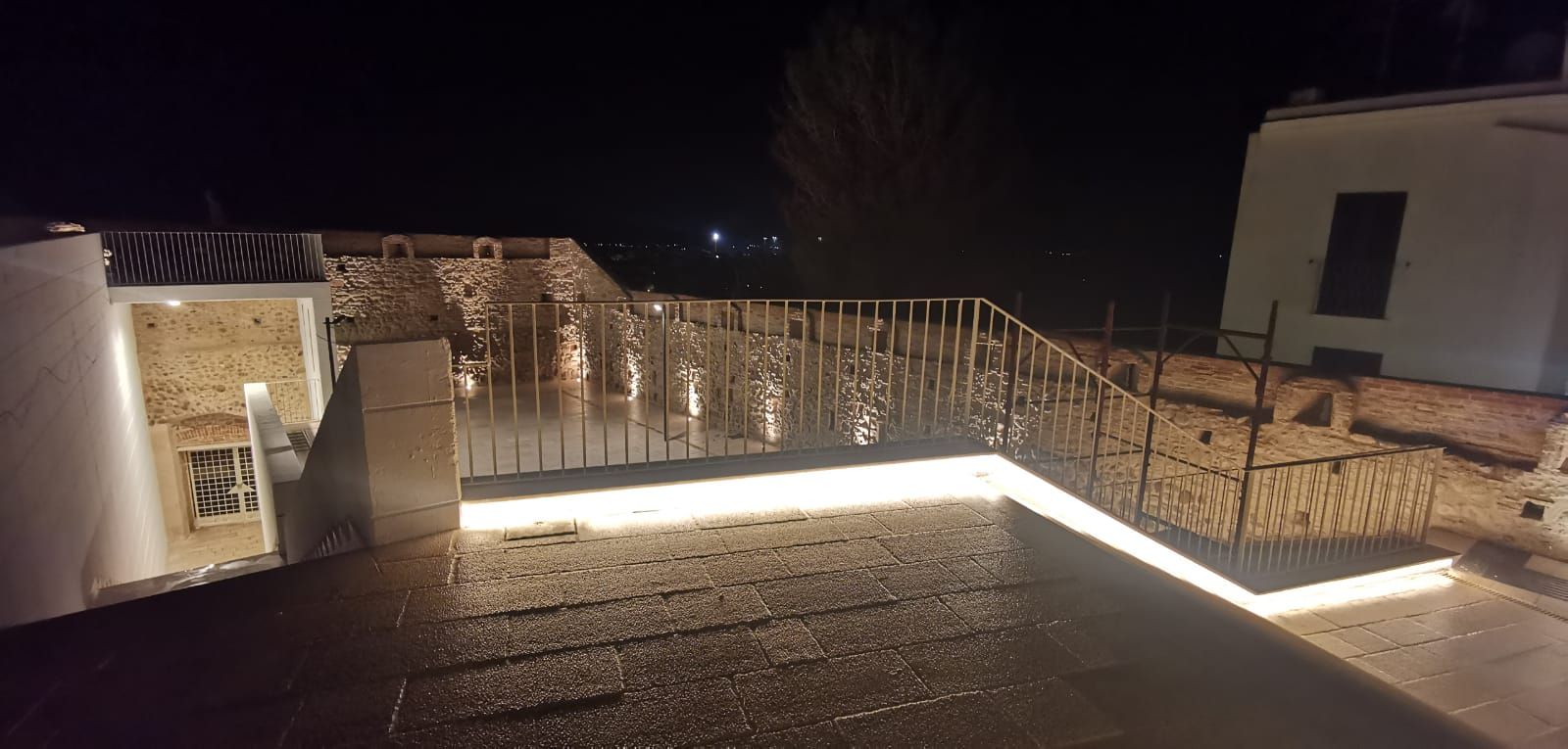 Ripresa notturna di un tetto con ringhiera illuminata e luci lungo il bordo.