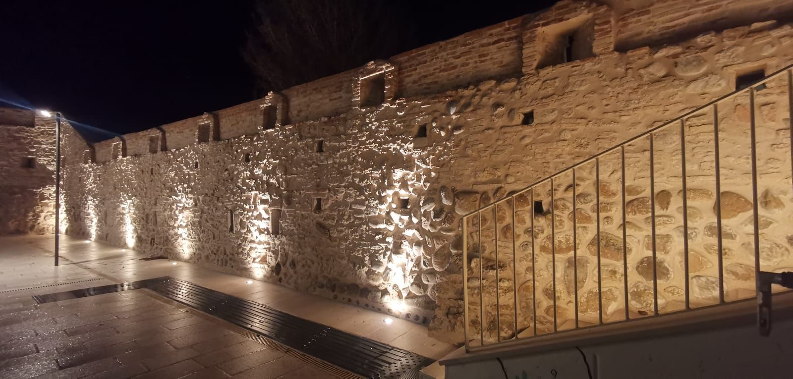 Edificio in pietra illuminato di notte da una ringhiera metallica.