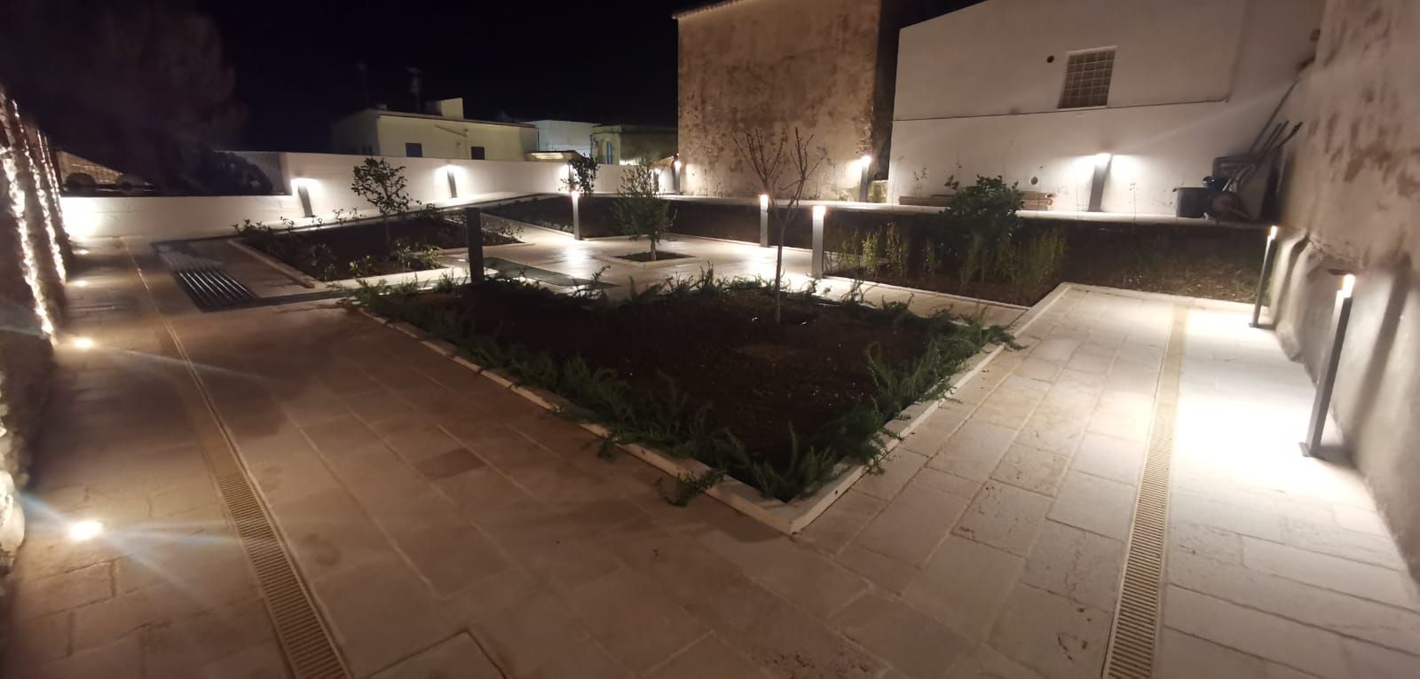 Vista notturna di un cortile pavimentato con edifici e paesaggi illuminati.