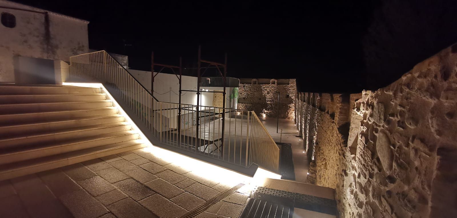 Vista notturna di una scala in pietra con illuminazione moderna, che conduce a un sentiero con muro in pietra.