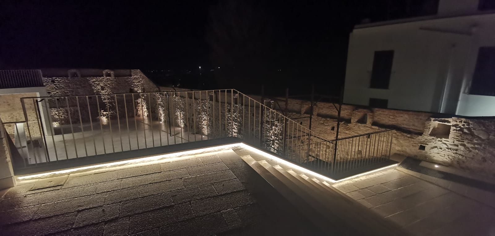 Patio sul tetto illuminato di notte. Recinzione decorativa con luci a stringa, bordi illuminati, sfondo scuro.