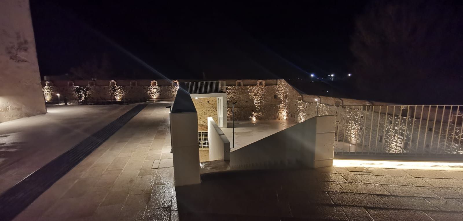 Vista notturna di una terrazza moderna con luci che illuminano pareti e camminamenti.