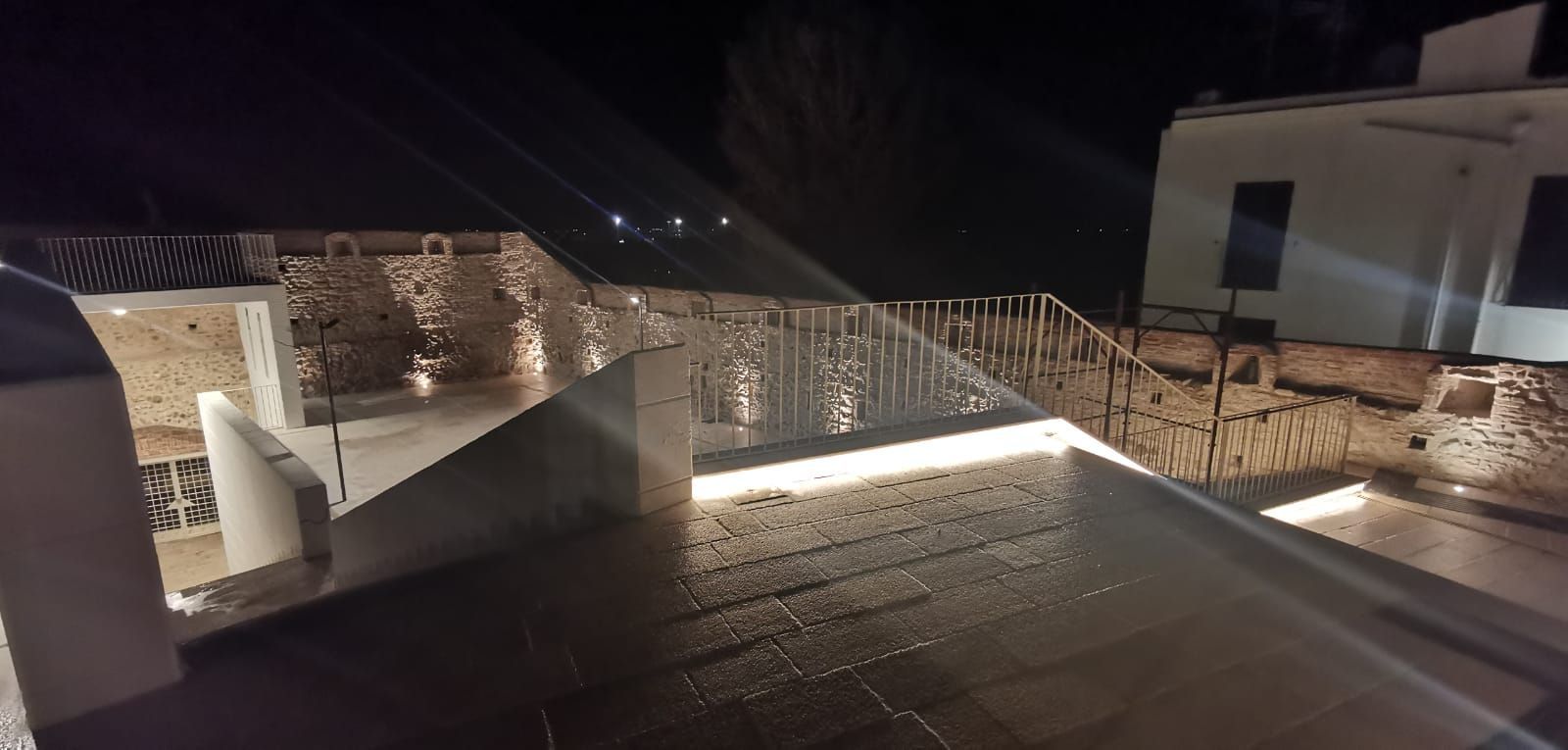 Vista notturna di un edificio con muri in pietra e una moderna ringhiera illuminata.