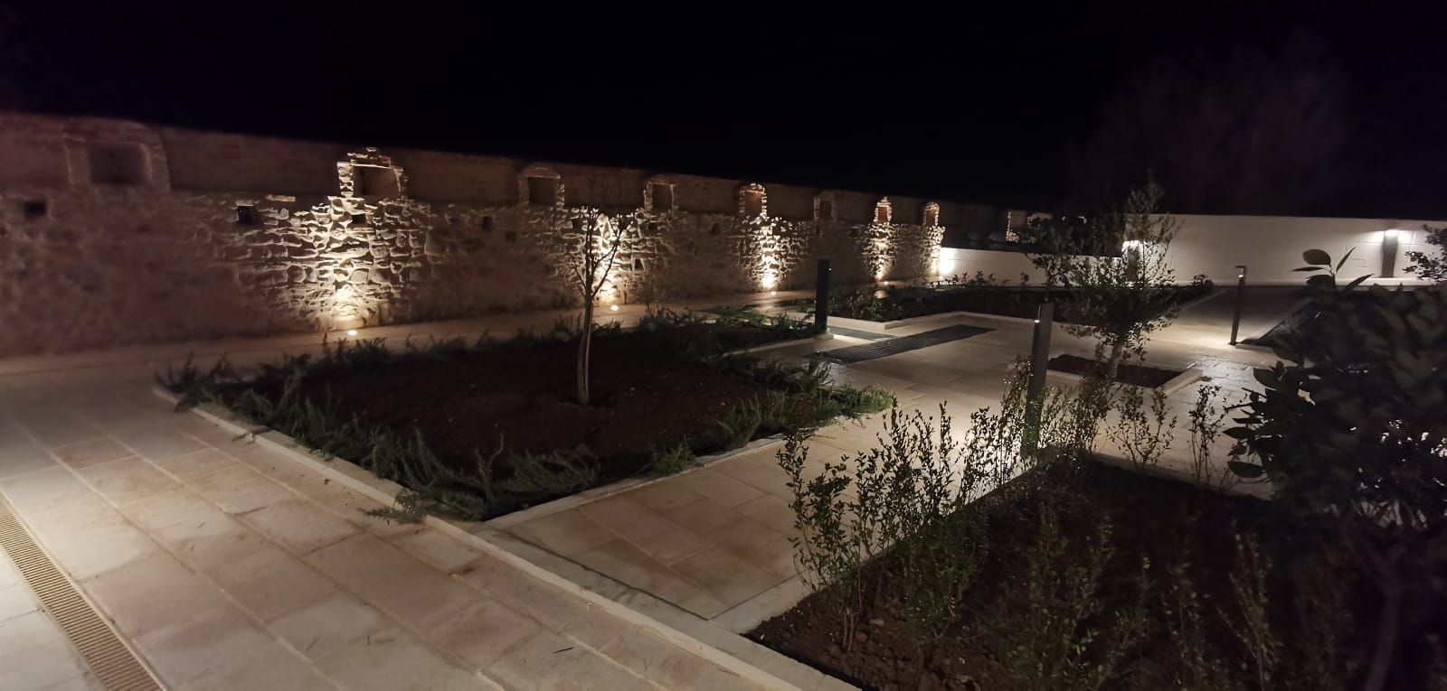 Vista notturna di un cortile con muri in pietra illuminati e paesaggio.