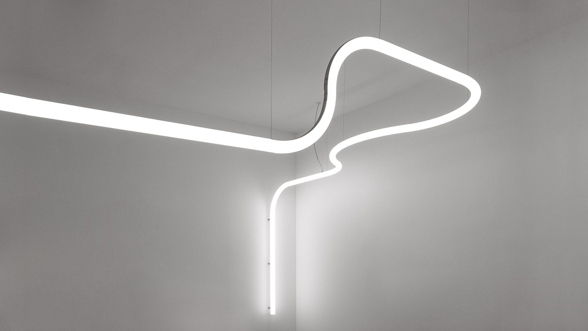 Una moderna lampada a LED bianca e curva è appesa a una parete semplice.