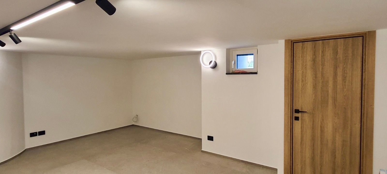 Stanza vuota con pareti bianche, una porta di legno e una piccola finestra.