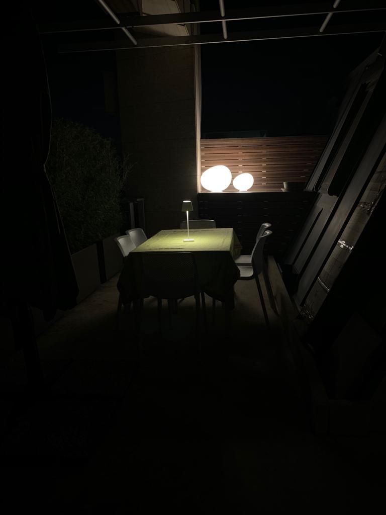 Patio esterno buio con un tavolo apparecchiato per cenare, illuminato da lampade.