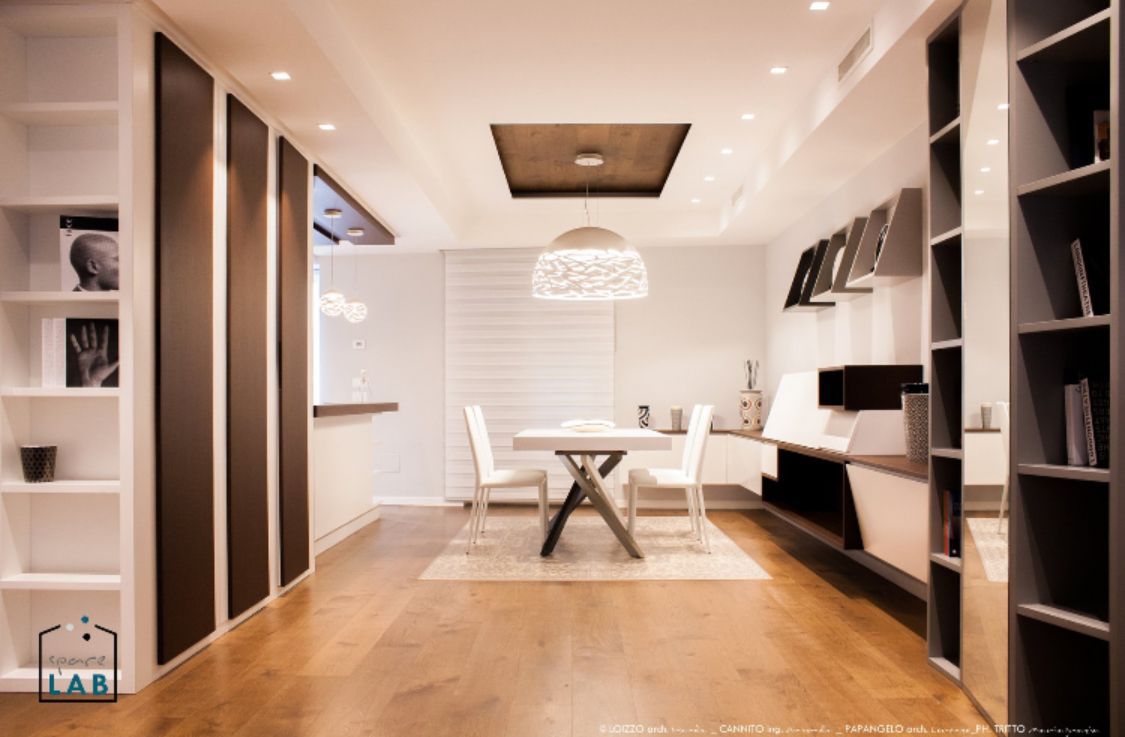 Moderna sala da pranzo con pareti bianche, pavimento in legno e scaffalature integrate.