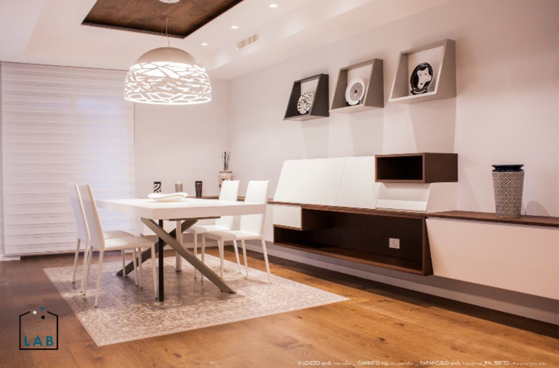 Moderna sala da pranzo con tavolo bianco, sedie e lampadario decorativo. Contenitori integrati e opere d'arte.
