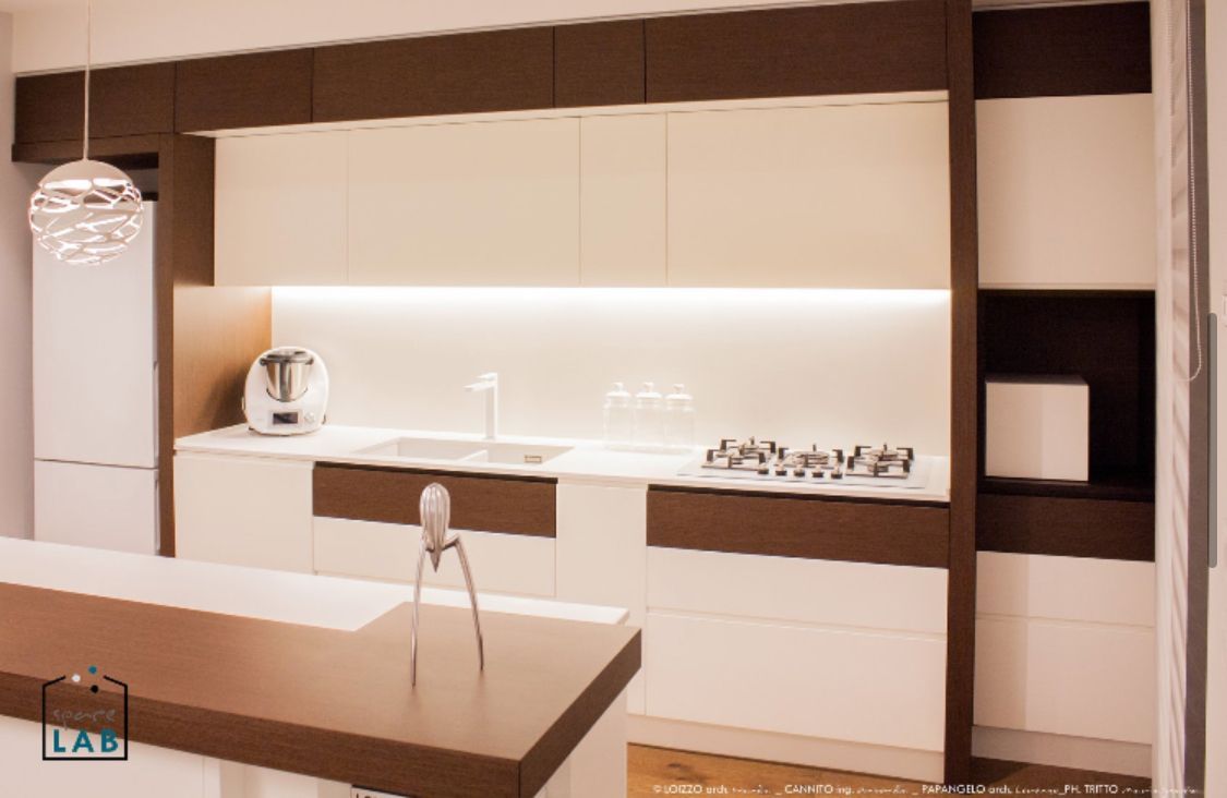 Cucina moderna con mobili bianchi e marroni, elettrodomestici in acciaio inossidabile e piano di lavoro.