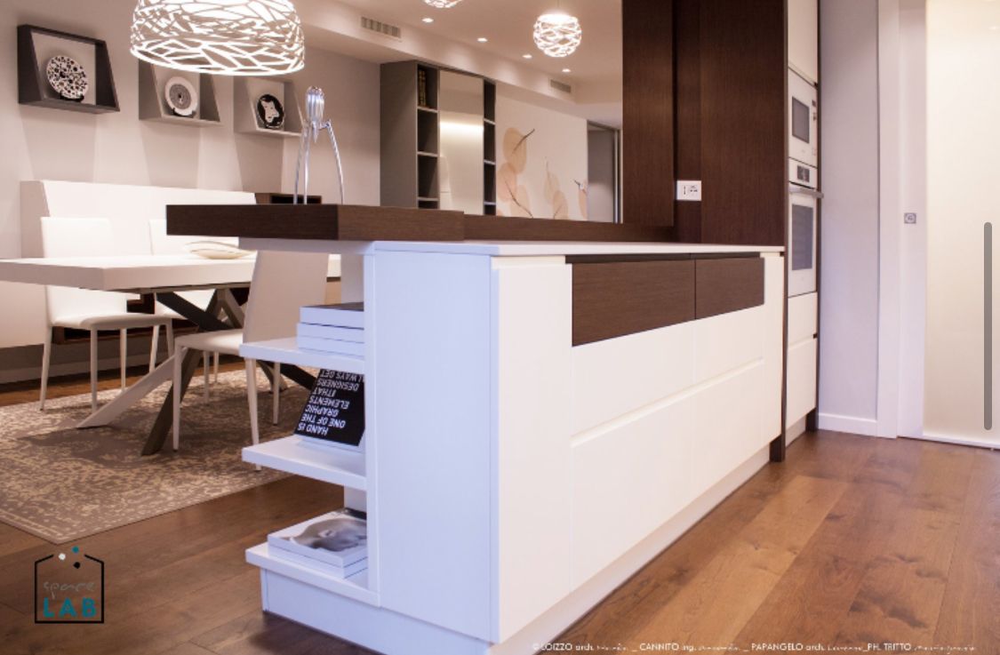 Moderna isola da cucina con mobili bianchi, piano di lavoro scuro e ripiani a vista.