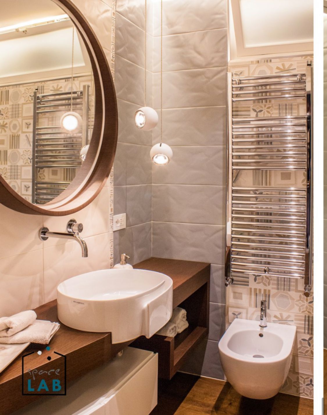 Bagno moderno con specchio rotondo, lavabo sospeso e piastrelle decorative.