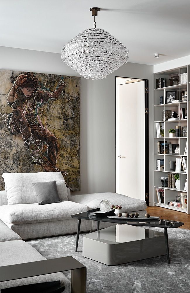 Soggiorno con divano bianco, quadri, lampadario e libreria.