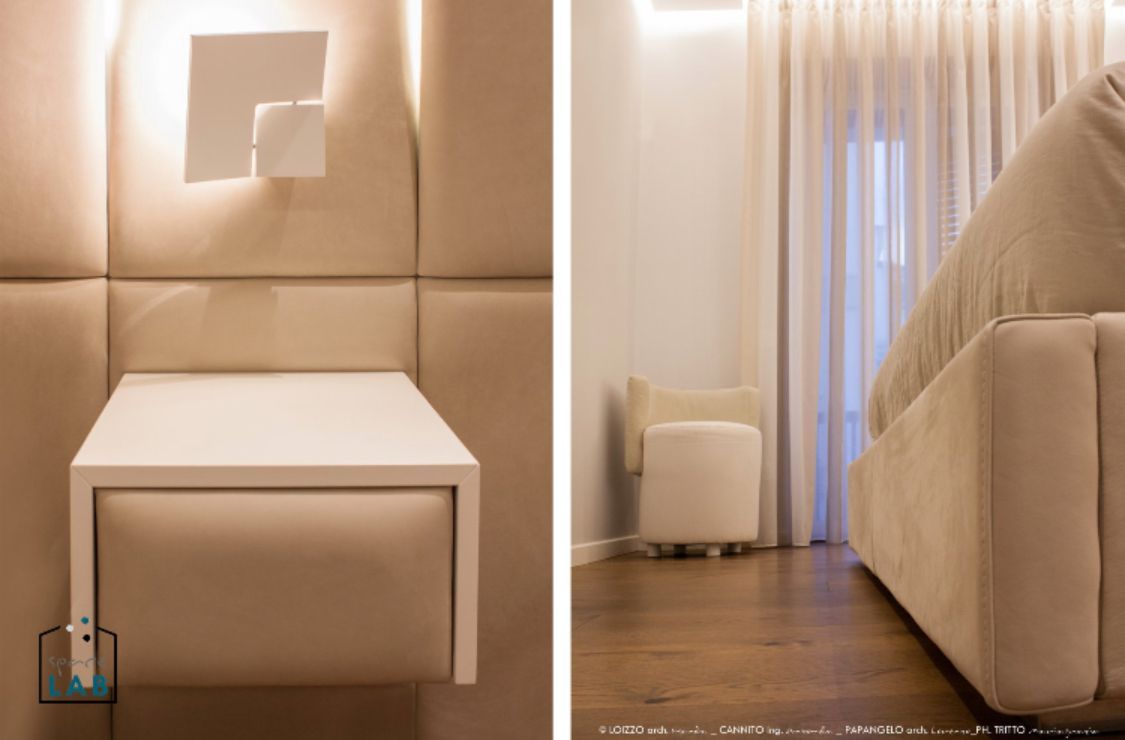 Camera da letto con comodino sospeso, applique, letto e tende trasparenti. Tenui toni beige.