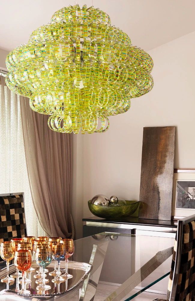 Lampadario verde sopra un tavolo da pranzo apparecchiato con bicchieri. Sono visibili opere d'arte marroni e una ciotola verde.