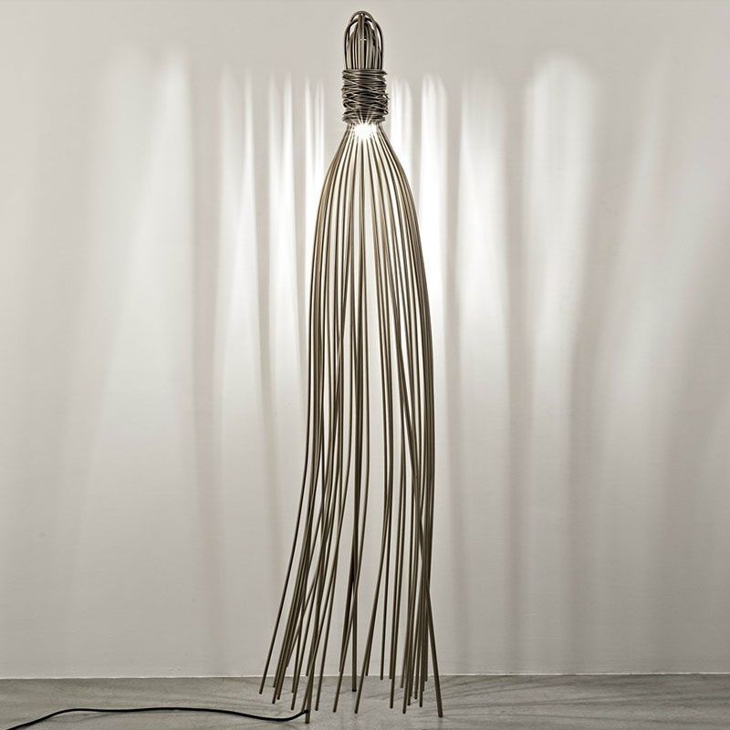 Lampada da terra in metallo argentato con numerose aste verticali che proiettano giochi di luce su una parete bianca.