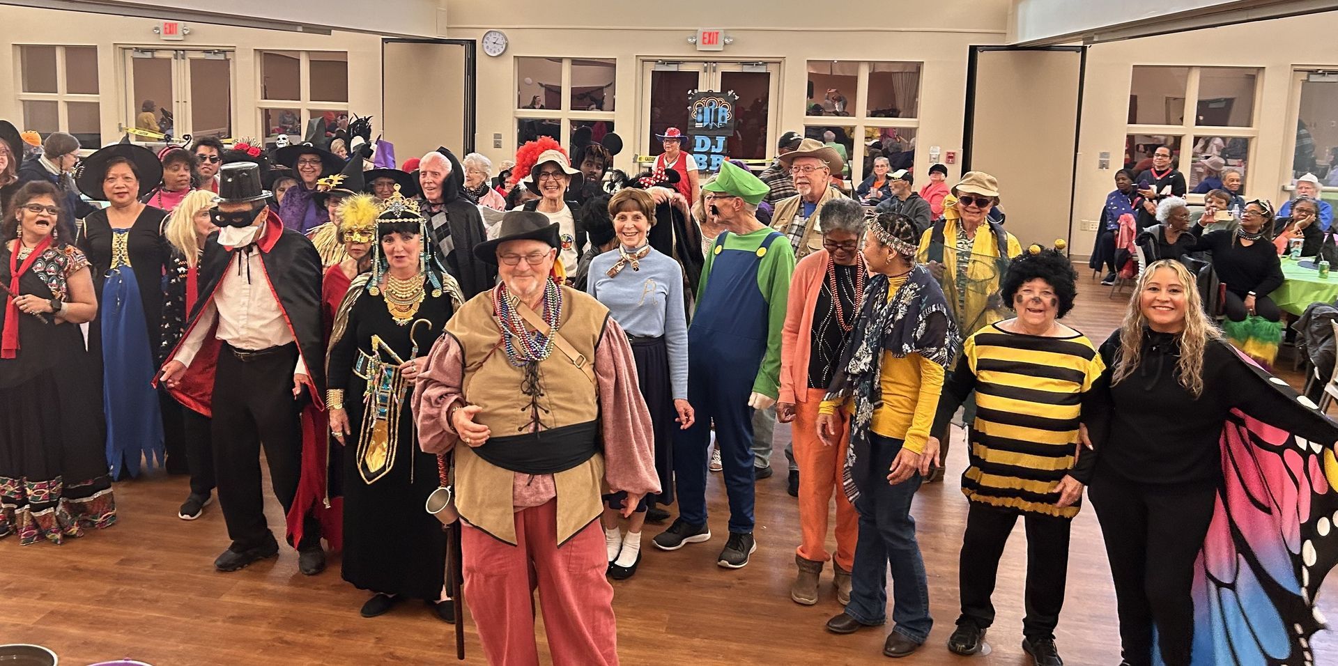 A large group of people in diverse costumes, including a bee and a butterfly, posing together in a large event room.