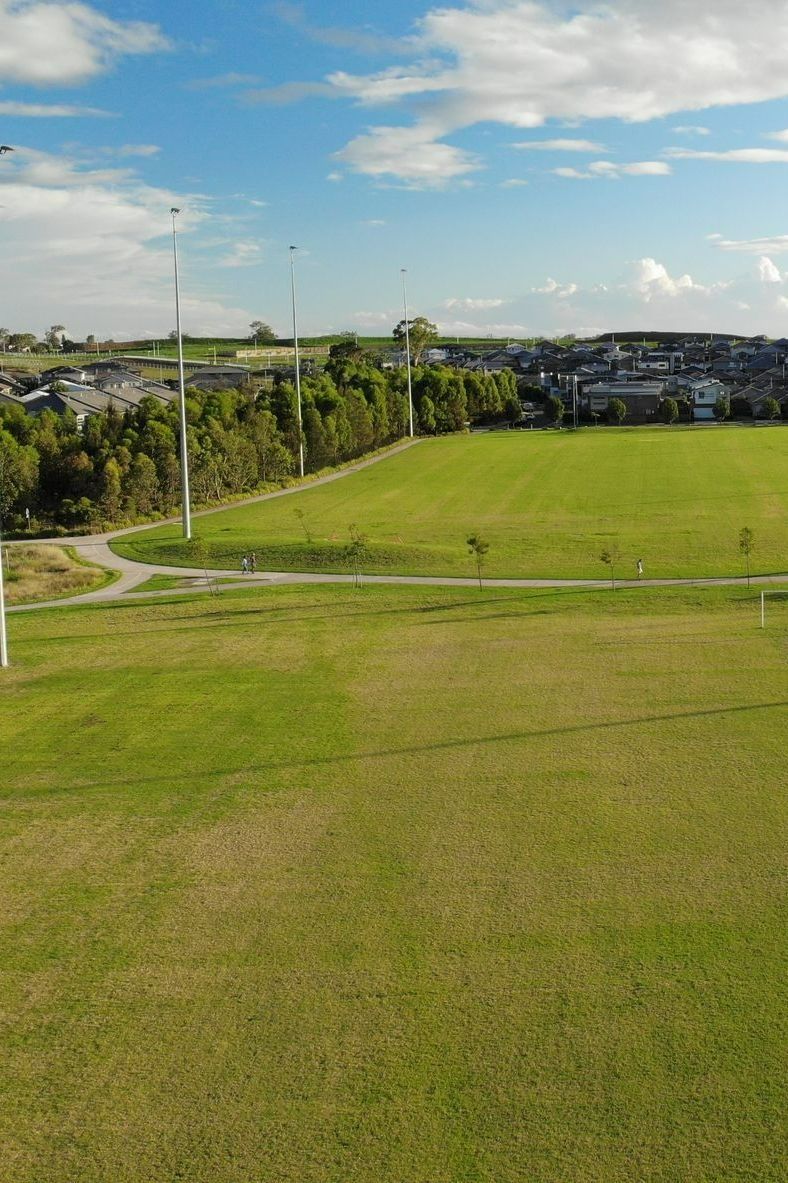 An aerial view of a green grassy field bordering a line of trees and a path — Ballina Turf Farm in Iluka, NSW