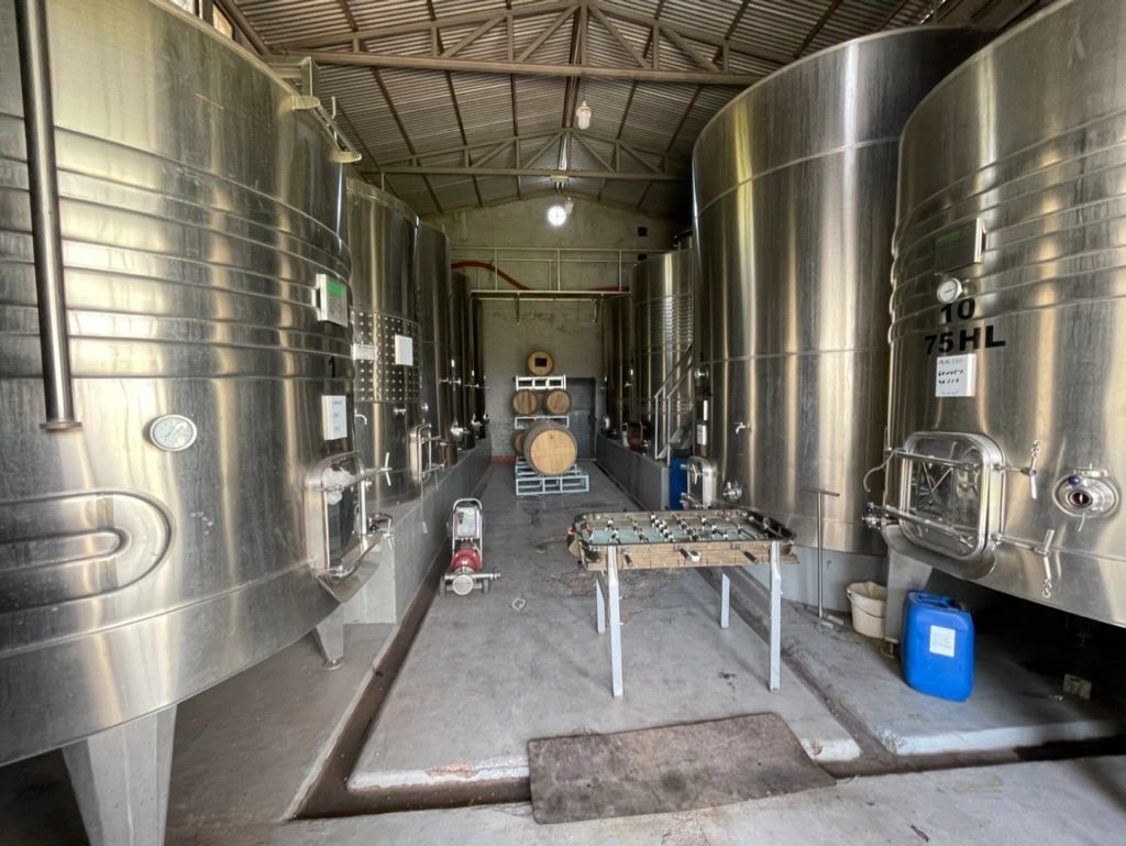 Large stainless steel tanks inside an industrial brewery or winery cellar with a concrete floor