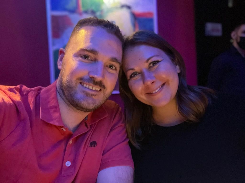 Two smiling people posing for a selfie in a dim, colorful indoor setting
