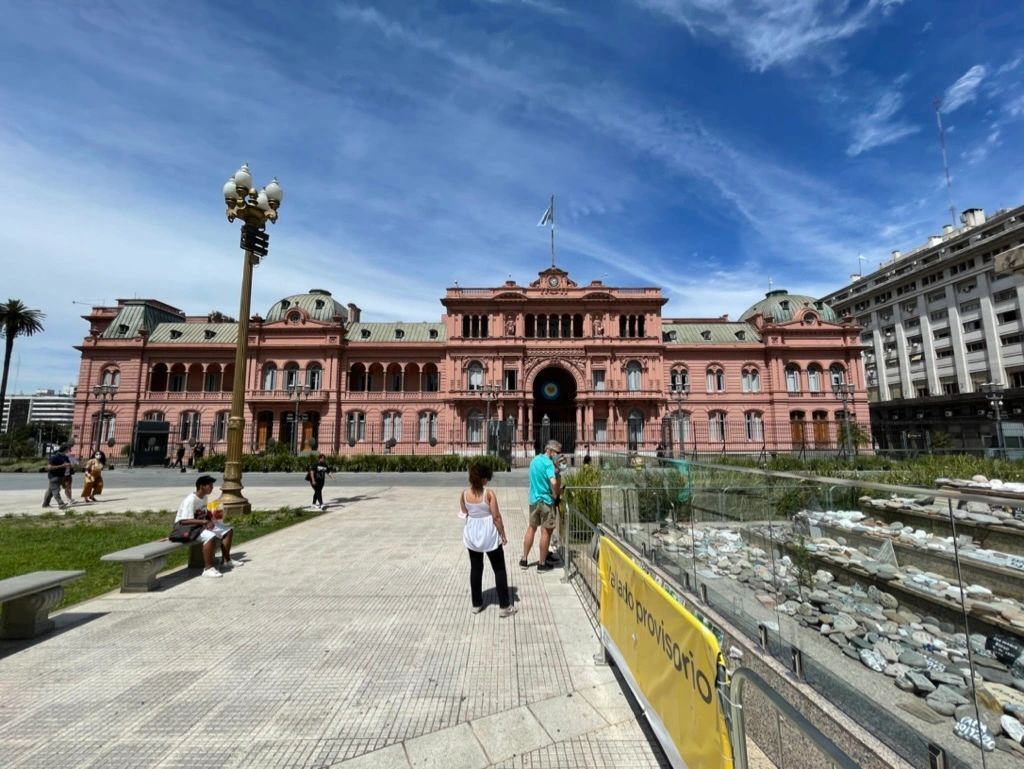 Pink historic building and plaza with a few people walking under a blue sky