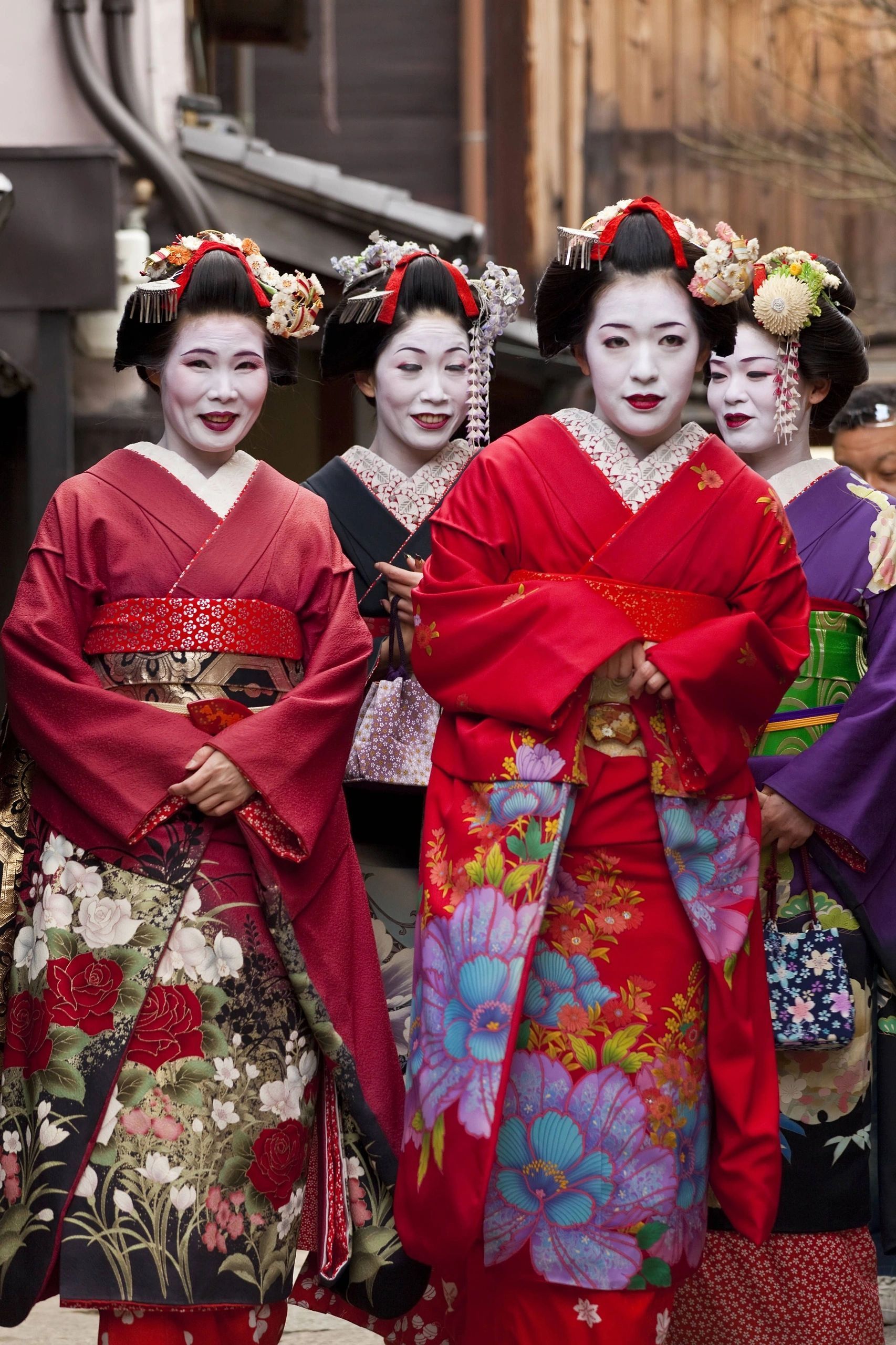 Four women in colorful kimonos and white makeup walk outdoors in a traditional Japanese setting