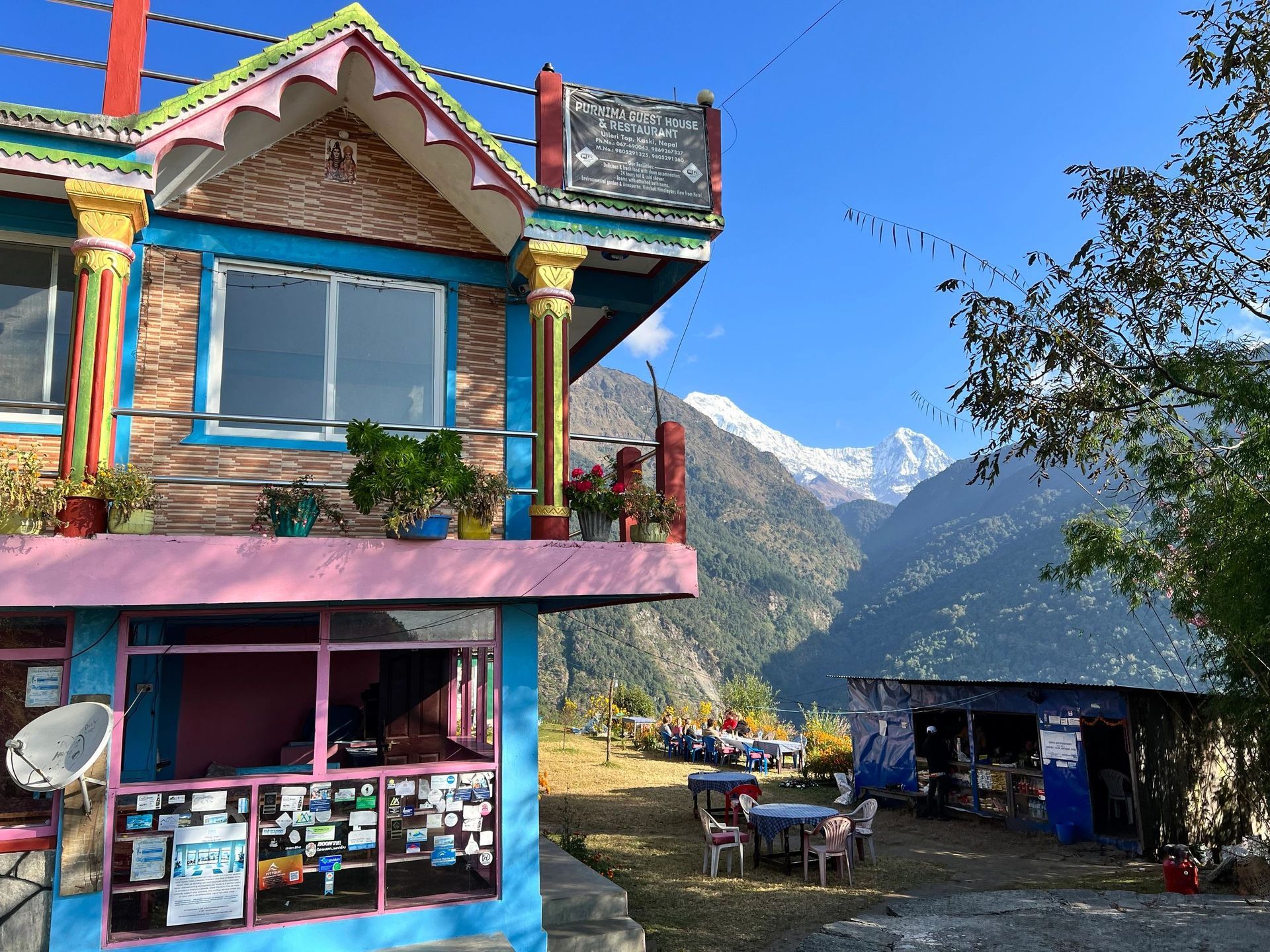 Colorful mountain guesthouse with patio seating and snowy peaks in the background