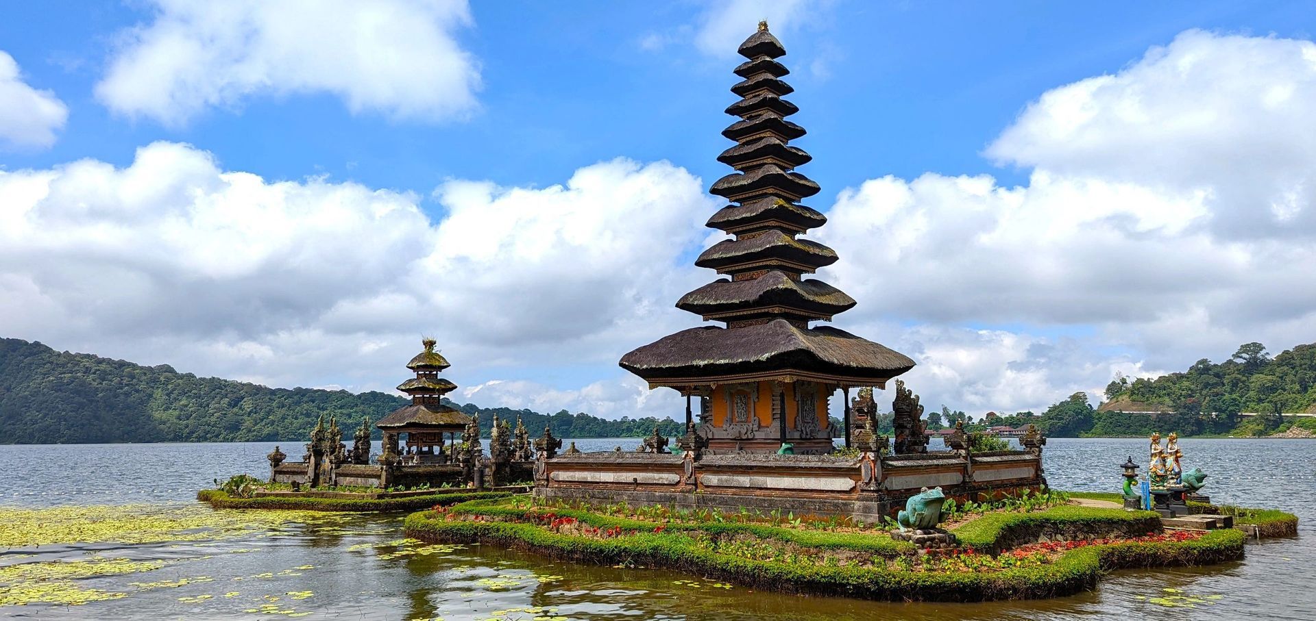 Balinese temple on a small island in a lake, with a tall pagoda and cloudy sky