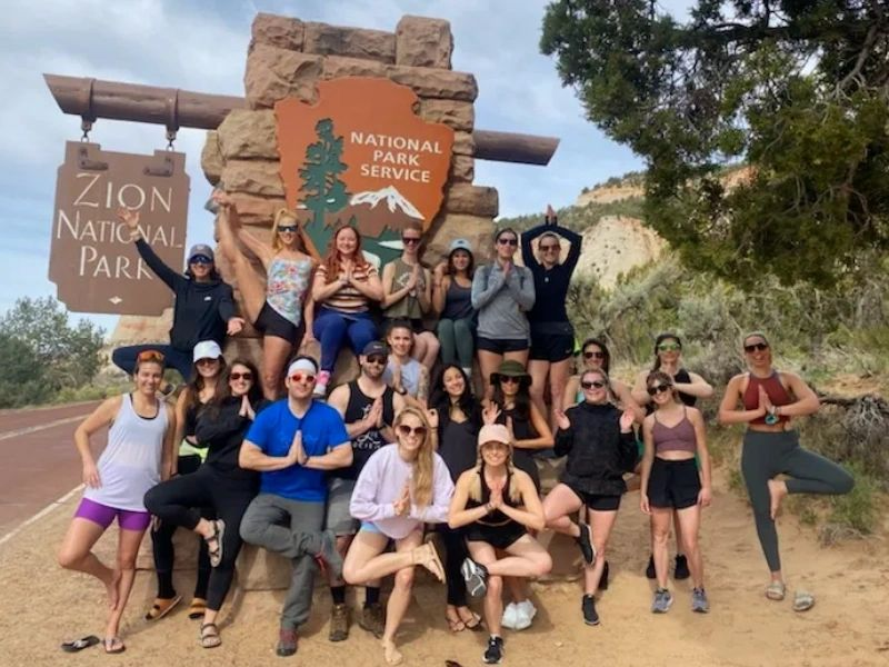 Group of hikers posing by Zion National Park sign on a desert roadside.