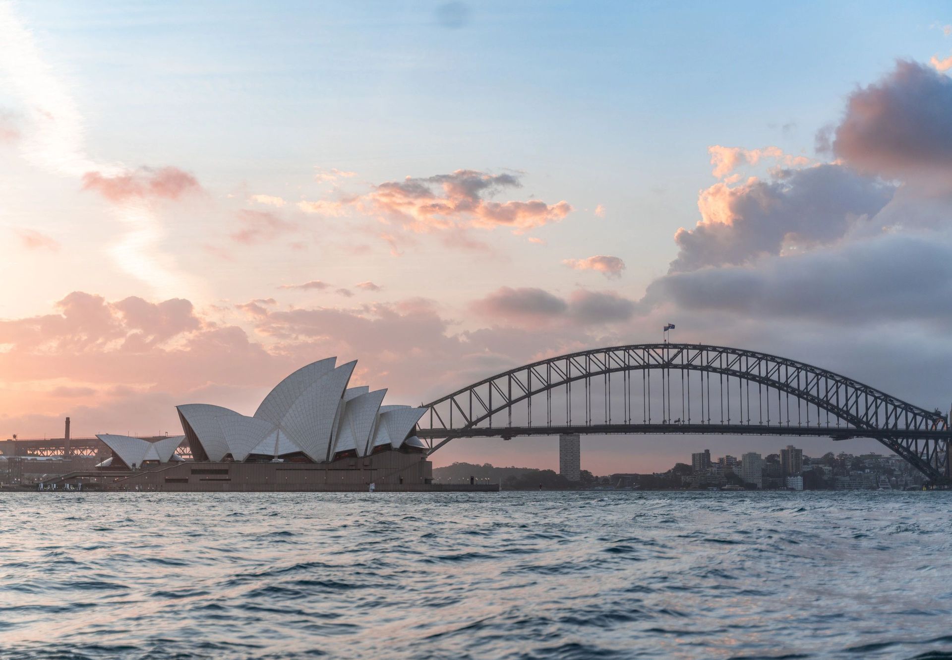 Sydney Opera House and Harbour Bridge at sunset over choppy water