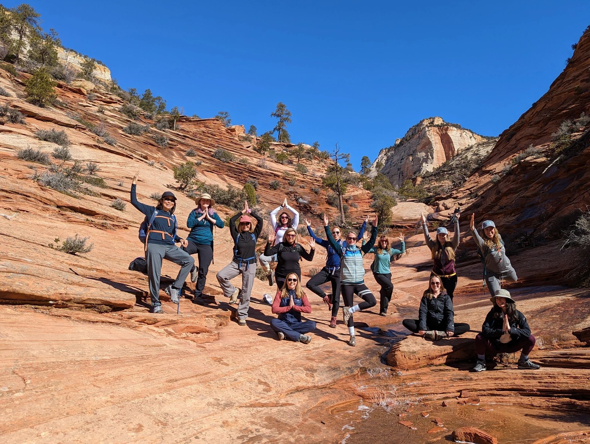 Group of hikers posing on a sunlit red-rock canyon trail under a blue sky