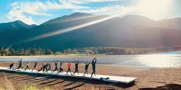People doing yoga on a dock by a mountain lake at sunrise
