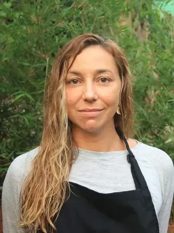 Portrait of a woman in a black apron against a leafy green background