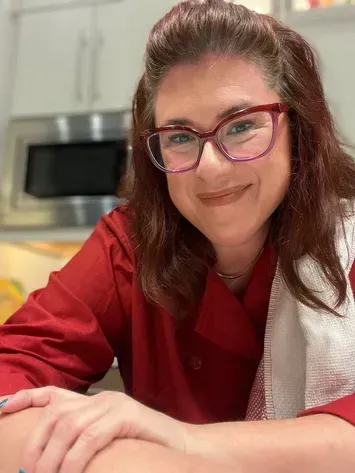 Smiling person in a red top and glasses sitting in a kitchen countertop.