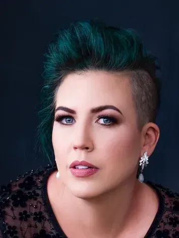 Portrait of a person with teal short hair and a black top against a dark background