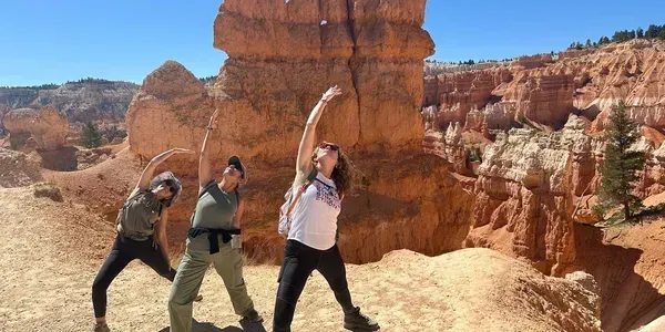 Three people posing with raised arms in a red rock canyon under a bright blue sky.