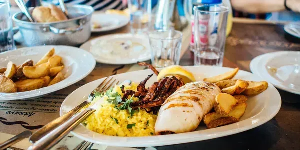 Plated seafood and rice on a dining table with fries and drinks in the background