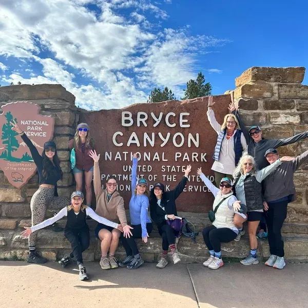 Group posing at Bryce Canyon National Park sign under a bright blue sky