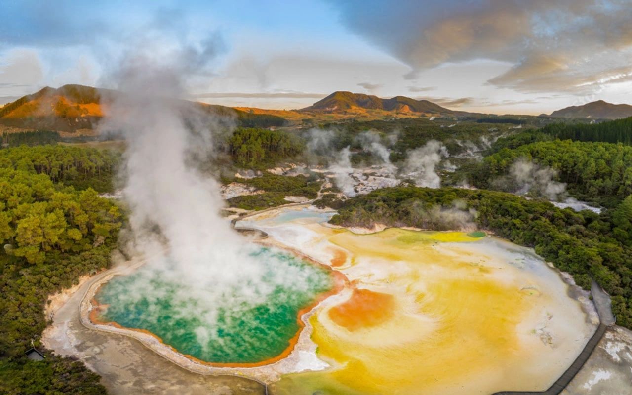Colorful geothermal hot spring with steaming turquoise and yellow pools in a forested landscape