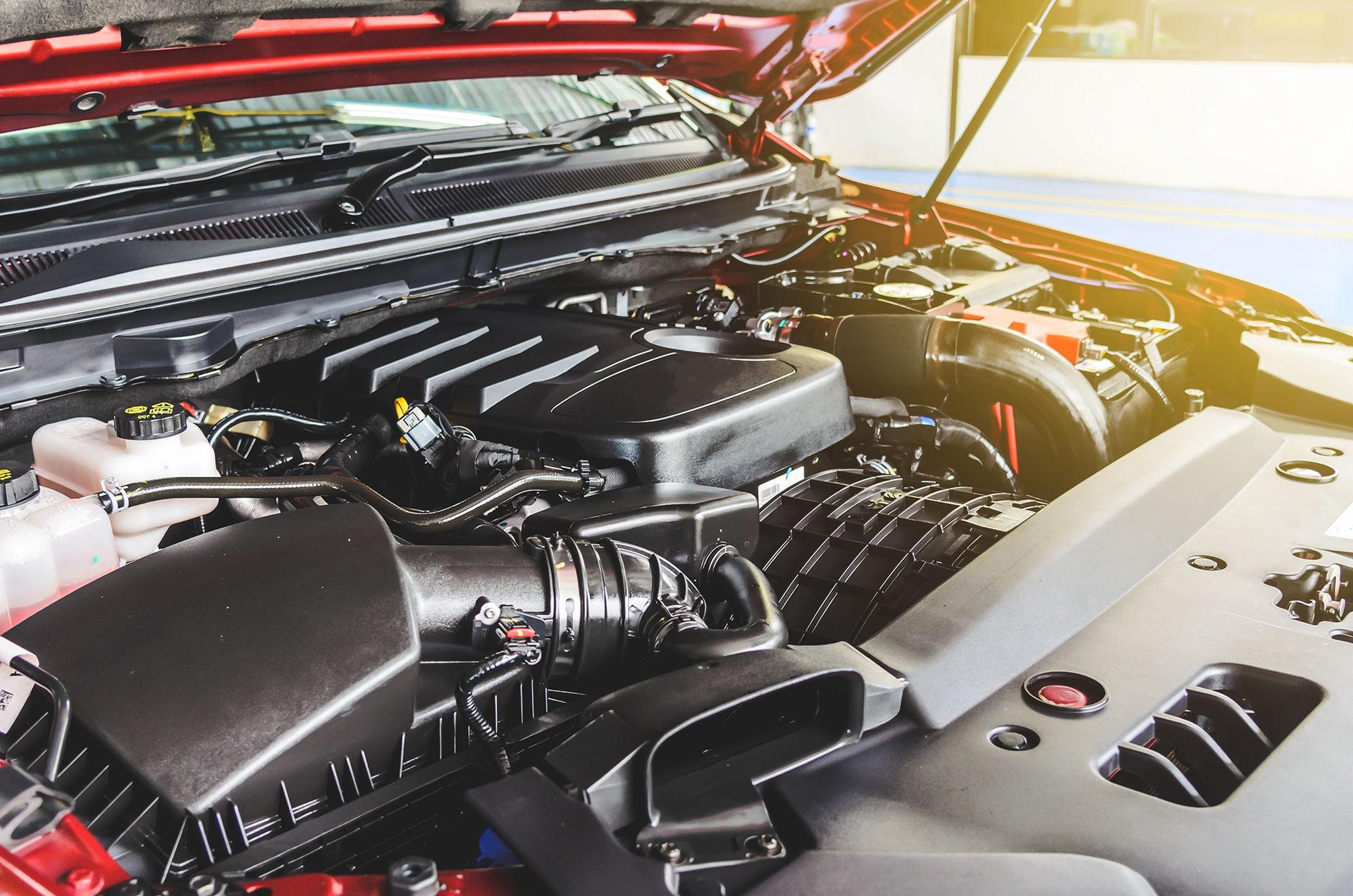 Open car hood showing a clean engine bay with black engine components and orange sunlight at the front right
