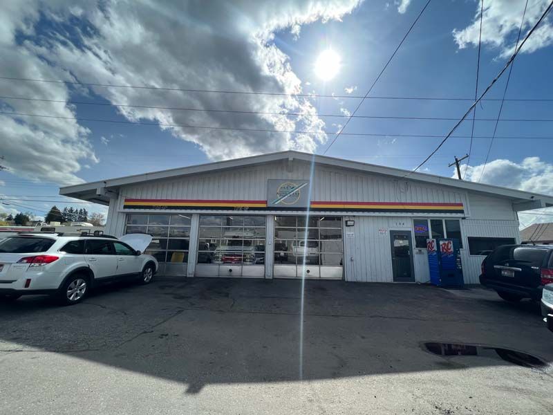 Small white storefront with parked cars and blue sky with clouds above