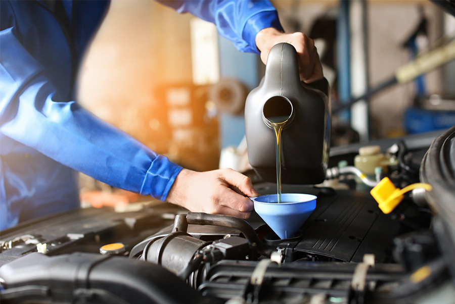 Mechanic pouring engine oil from a black jug into a funnel under the hood of a car