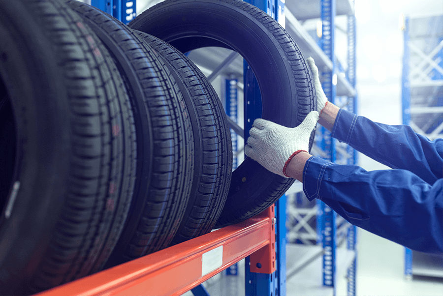 Gloved hands inspecting stacked black tires on a red warehouse rack