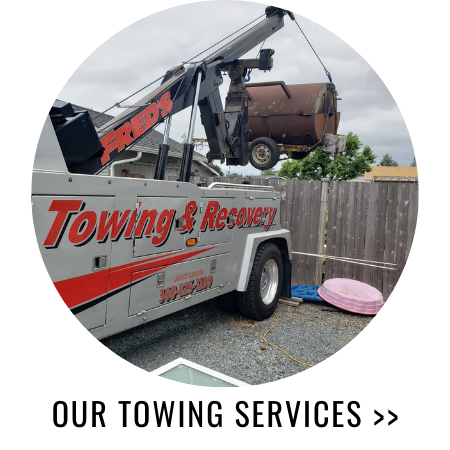 Tow truck lifting a rusty metal object from a gravel area.