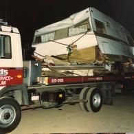 A damaged trailer is loaded on a tow truck at night.
