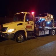 A tow truck with a Jeep on its flatbed at night.